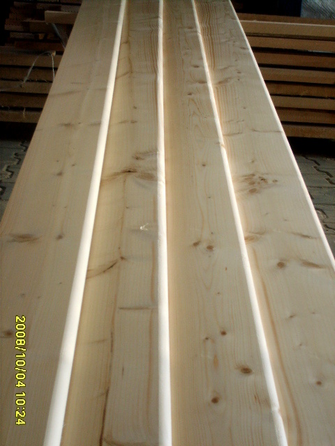 Stos jasnych, sosnowych desek elewacyjnych typu klin, ułożonych jedna na drugiej, widoczne sęki i naturalny rysunek drewna.