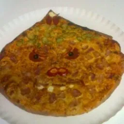 Nietypowa pizza na papierowym talerzu, ułożona tak, by przypominała twarz z pepperoni jako oczami i ketchupem jako ustami.