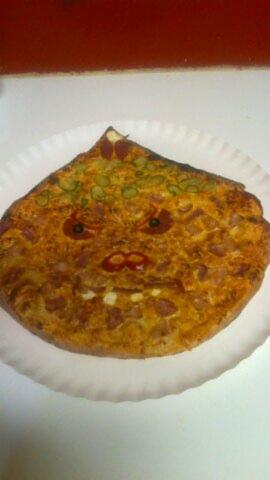 Nietypowa pizza na papierowym talerzu, ułożona tak, by przypominała twarz z pepperoni jako oczami i ketchupem jako ustami.