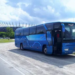 Niebieski autokar turystyczny z otwartymi drzwiami na tle Stadionu Narodowego w Warszawie, z widocznym logo firmy Club Bus i polską flagą na przedniej szybie.