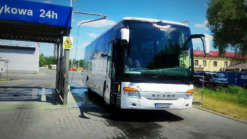 Autokar marki Setra po myciu w myjni automatycznej, widoczne krople wody na karoserii, znak ostrzegawczy na słupie.