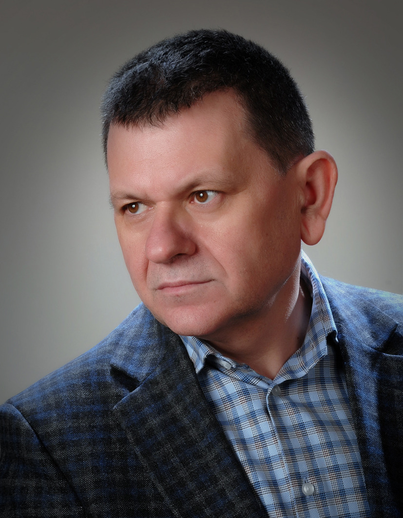 Portret mężczyzny w niebieskiej koszuli w kratę i tweedowej marynarce, spoglądającego w lewo, na szarym tle.