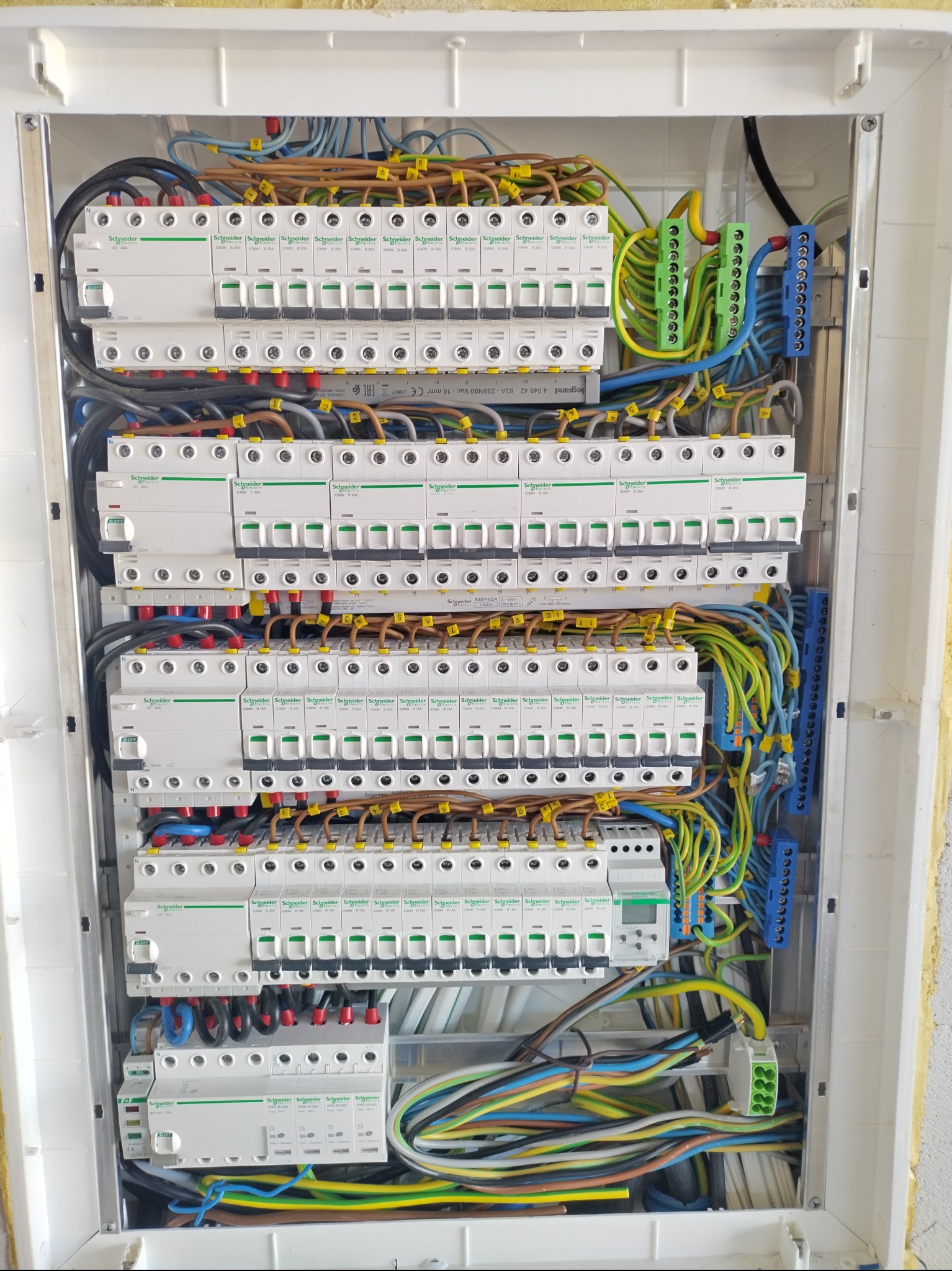 Otwarta skrzynka elektryczna z zainstalowanymi bezpiecznikami Schneider Electric, różnokolorowymi przewodami oznaczonymi numerami i złączkami, widoczne elementy montażowe i okablowanie.
