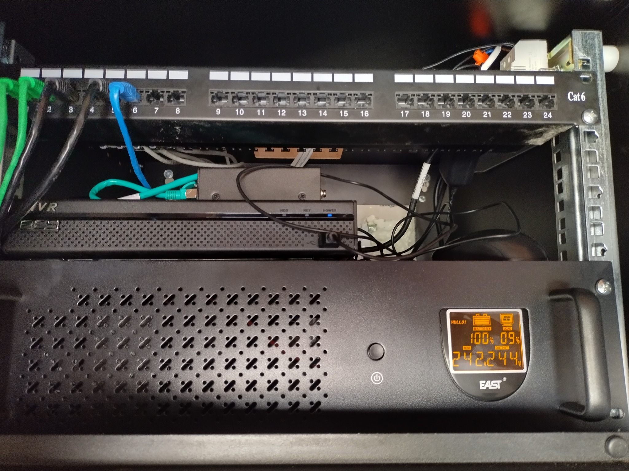 Panel krosowniczy Cat 6 z podłączonymi kablami sieciowymi, zamontowany w szafie rack, poniżej widoczny zasilacz awaryjny UPS marki EAST z wyświetlaczem informującym o stanie naładowania baterii...