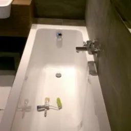 Biała wanna po renowacji z narzędziami malarskimi w środku. Szare płytki na ścianach i drewniany element umywalki. Widok z góry na wykończoną łazienkę.