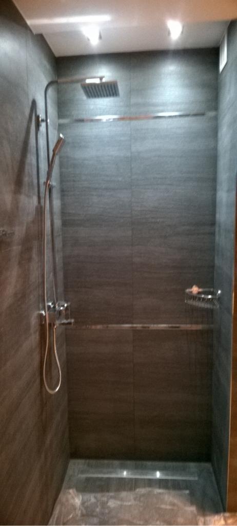 Nowoczesna kabina prysznicowa z szarymi płytkami imitującymi drewno, deszczownicą i odpływem liniowym, zabezpieczona folią ochronną.