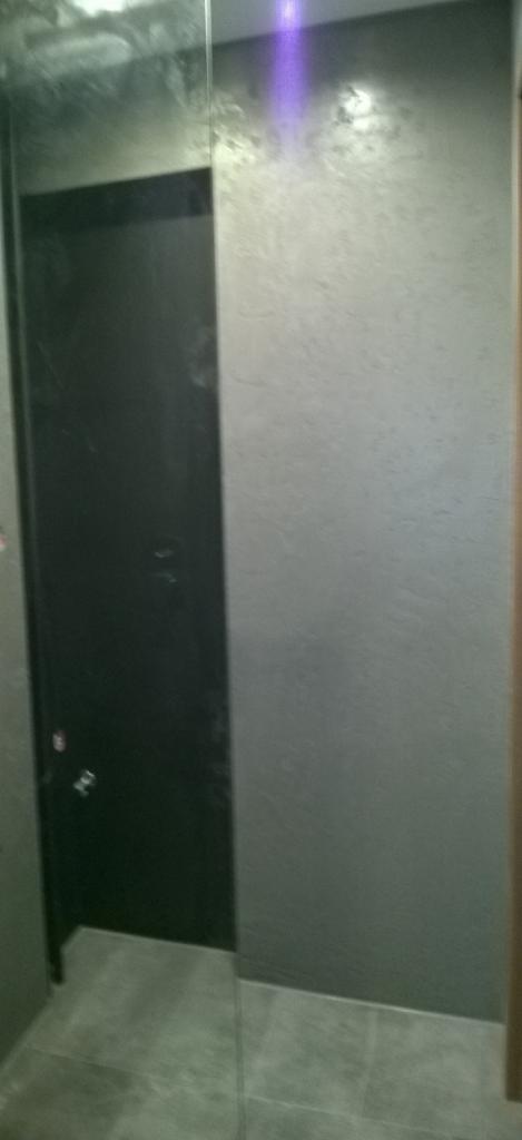 Nowoczesna łazienka z kabiną prysznicową typu walk-in i szarą, teksturowaną ścianą. Minimalistyczny design z płytkami podłogowymi w odcieniach szarości.