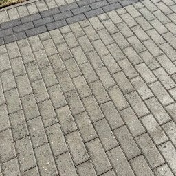 SERVICE CONSTRUCTION Sp. z o.o. - Ułożona kostka brukowa w odcieniach szarości, z pasem ciemniejszej kostki przy krawędzi trawnika, widziana pod kątem.