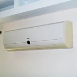 Biały klimatyzator Galanz zamontowany na jasnej ścianie w biurze, widoczny fragment okna z zasłoną i karnisz.