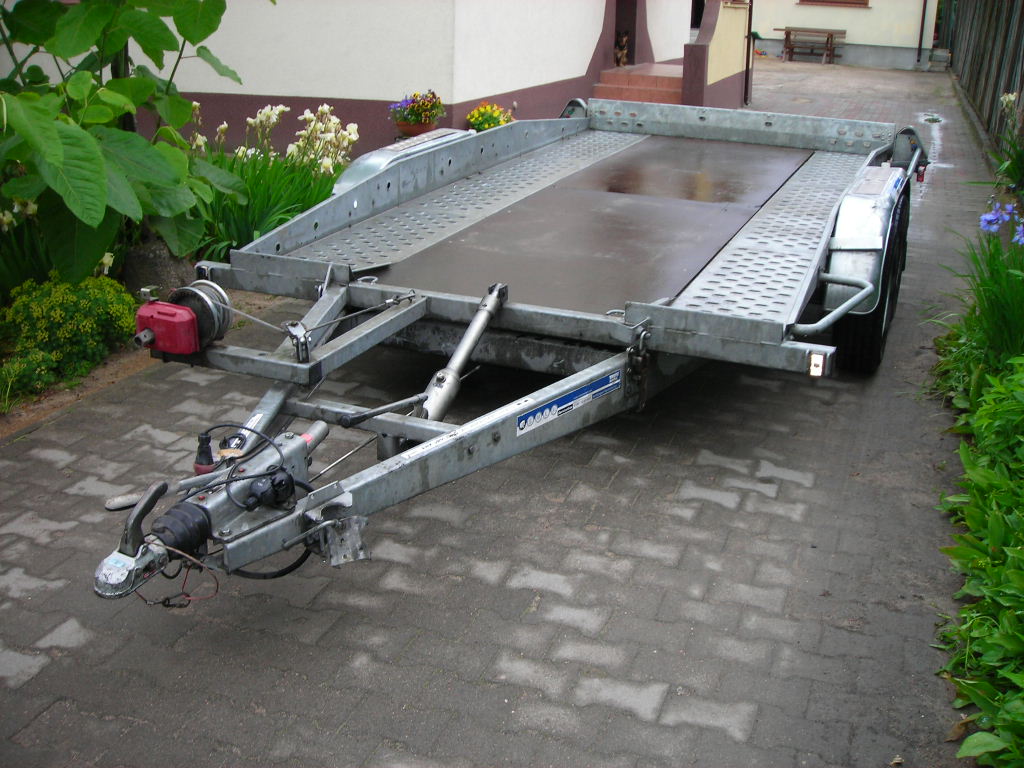 Pusta, dwuosiowa laweta samochodowa z wyciągarką, zaparkowana na brukowanym podjeździe w Lubinie, gotowa do transportu pojazdów.