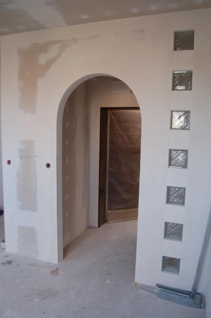 Ściana działowa z płyty karton-gips z łukowym przejściem i dekoracyjnymi luksferami, widoczne ślady szpachlowania i przygotowania do malowania.