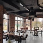 Loftowe wnętrze restauracji w Rumi z widoczną instalacją wentylacyjną pod sufitem, ceglanymi ścianami i dużymi oknami.