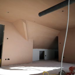 RAFFENER Rafał Jasiukajć - Wnętrze po szpachlowaniu: gładkie, beżowe ściany i sufit poddasza z widocznymi otworami na gniazdka elektryczne. W tle widoczne surowe otwory drzwiowe.