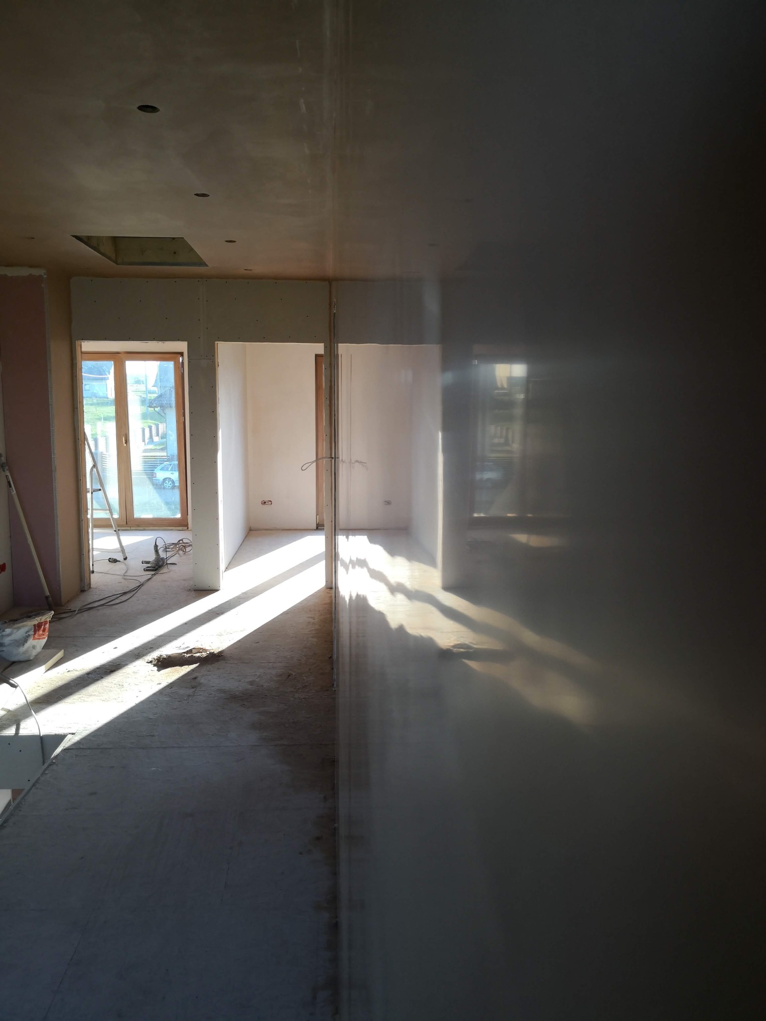 Wnętrze w trakcie remontu: gładkie, jasne ściany po szpachlowaniu, widoczne okno z promieniami słońca, surowy beton na podłodze. Prace wykończeniowe w nowym domu.