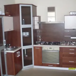 Kompletna zabudowa kuchenna z brązowymi frontami i srebrnymi detalami, obejmująca szafki wiszące, stojące, piekarnik i płytę gazową, uzupełniona o srebrny okap i akcesoria kuchenne na blacie.