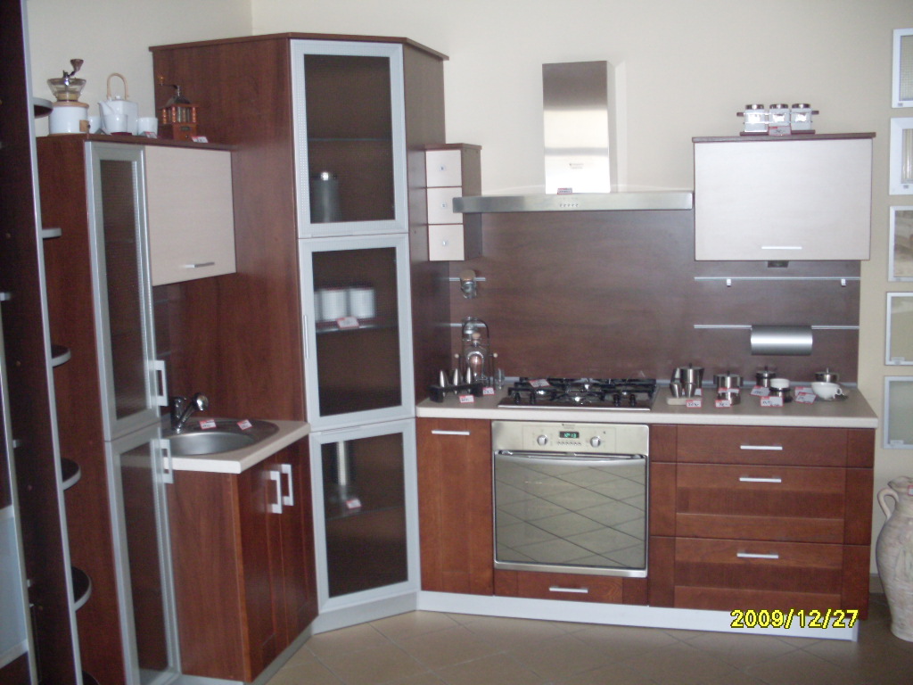 Kompletna zabudowa kuchenna z brązowymi frontami i srebrnymi detalami, obejmująca szafki wiszące, stojące, piekarnik i płytę gazową, uzupełniona o srebrny okap i akcesoria kuchenne na blacie.