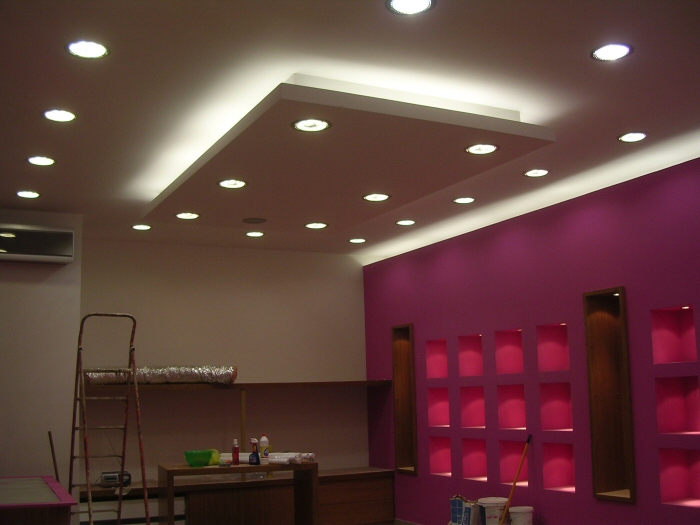 Wykończony sufit podwieszany z płyt gipsowo-kartonowych z wbudowanym oświetleniem punktowym, widoczna drabina i przygotowane ściany w kolorze fuksji z wnękami.