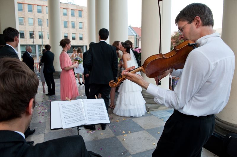 Skrzypek grający na skrzypcach podczas uroczystości ślubnej, w tle para młoda w trakcie pocałunku, nuty na pulpicie