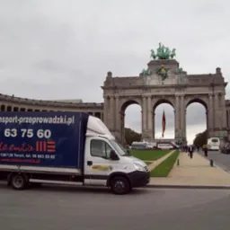Samochód dostawczy z reklamą firmy przeprowadzkowej na tle łuku triumfalnego w Brukseli. Widoczny adres strony www i numer telefonu.