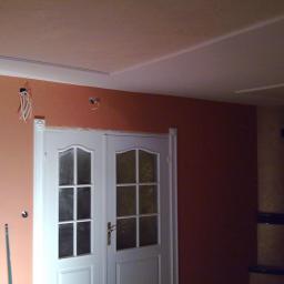 Veldecor - Ściana pomalowana na dwa kolory z widocznymi wystającymi przewodami elektrycznymi i podwójnymi białymi drzwiami z szybkami.