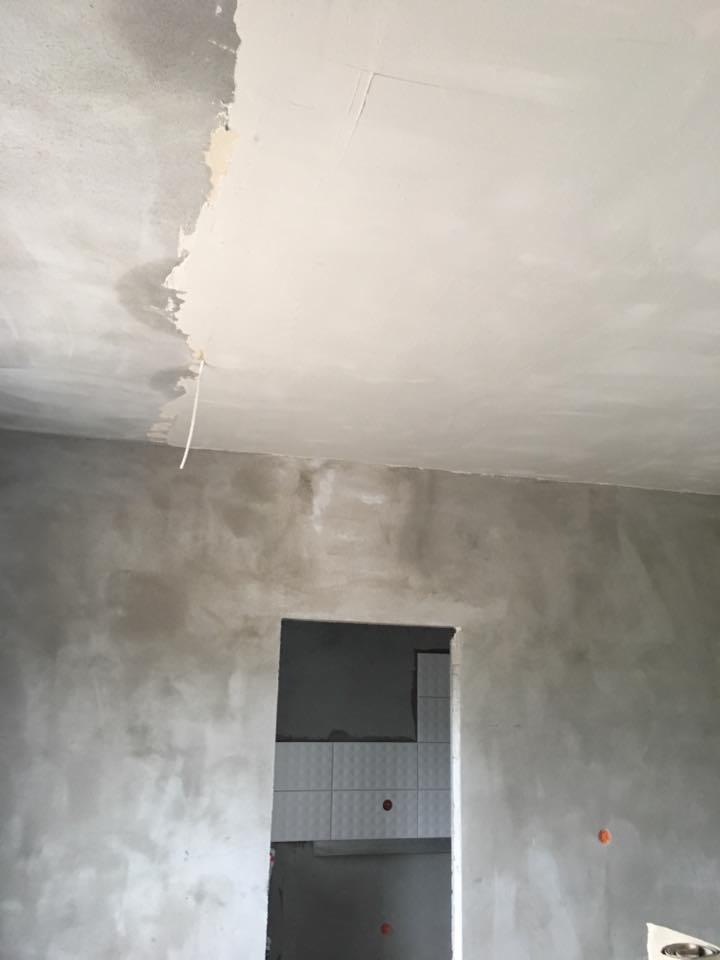 Ściana i sufit w trakcie prac wykończeniowych, widoczne nierówności i fragment położonej gładzi na suficie, w tle otwór drzwiowy z częściowo wykończoną łazienką.