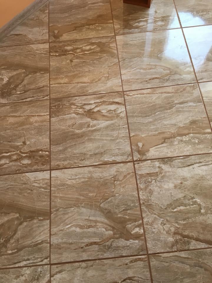 Błyszcząca, beżowo-brązowa podłoga z płytek imitujących marmur, ułożonych w regularny wzór z widocznymi fugami.