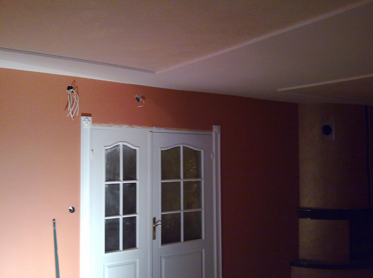 Ściana pomalowana na dwa kolory z widocznymi wystającymi przewodami elektrycznymi i podwójnymi białymi drzwiami z szybkami.