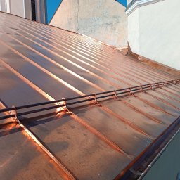 PRZEDSIĘBIORSTWO WIELOBRANŻOWE MARCIN BIENIO - Nowy, miedziany dach z systemem odśnieżania, widok z góry na tle miejskiej zabudowy.