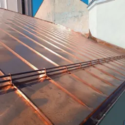 Nowy, miedziany dach z systemem odśnieżania, widok z góry na tle miejskiej zabudowy.