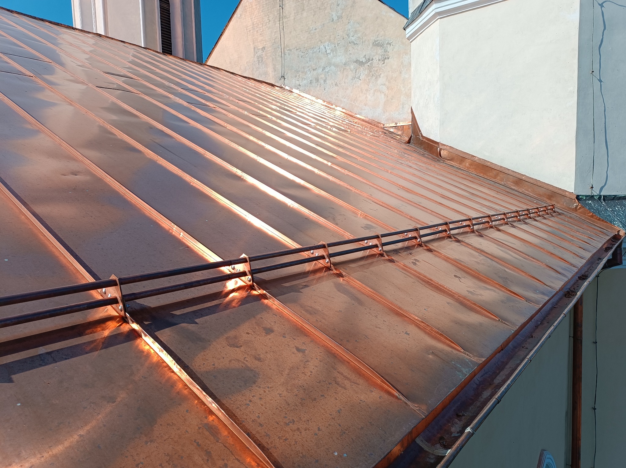 Nowy, miedziany dach z systemem odśnieżania, widok z góry na tle miejskiej zabudowy.