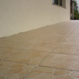 Wykafelkowany taras z beżowymi płytkami o nieregularnym wzorze, widok z boku, jasna elewacja budynku w tle.