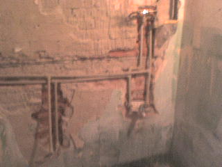 Odsłonięta instalacja elektryczna w ścianie podczas remontu, widoczne kable w bruzdach, ściana z resztkami tynku i fragmentami cegieł.