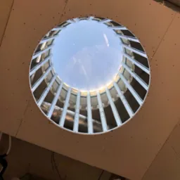 Okrągły otwór w suficie z płyty karton gips, widoczne metalowe profile i ocieplenie, niebo w tle.