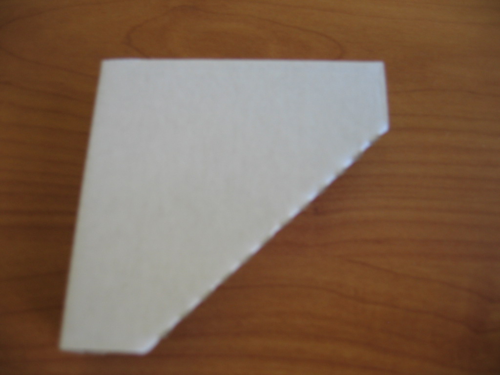 Biały, tekturowy narożnik ochronny, ułożony na drewnianym blacie, z widoczną strukturą tektury na krawędziach.