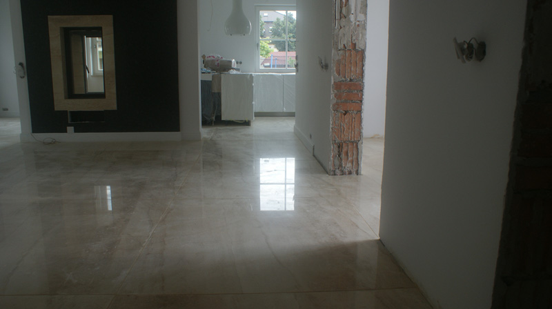 Wnętrze w trakcie wykańczania, z położoną marmurową posadzką, widoczne fragmenty niedokończonych ścian i instalacji elektrycznej, w tle okno i elementy wyposażenia kuchni.