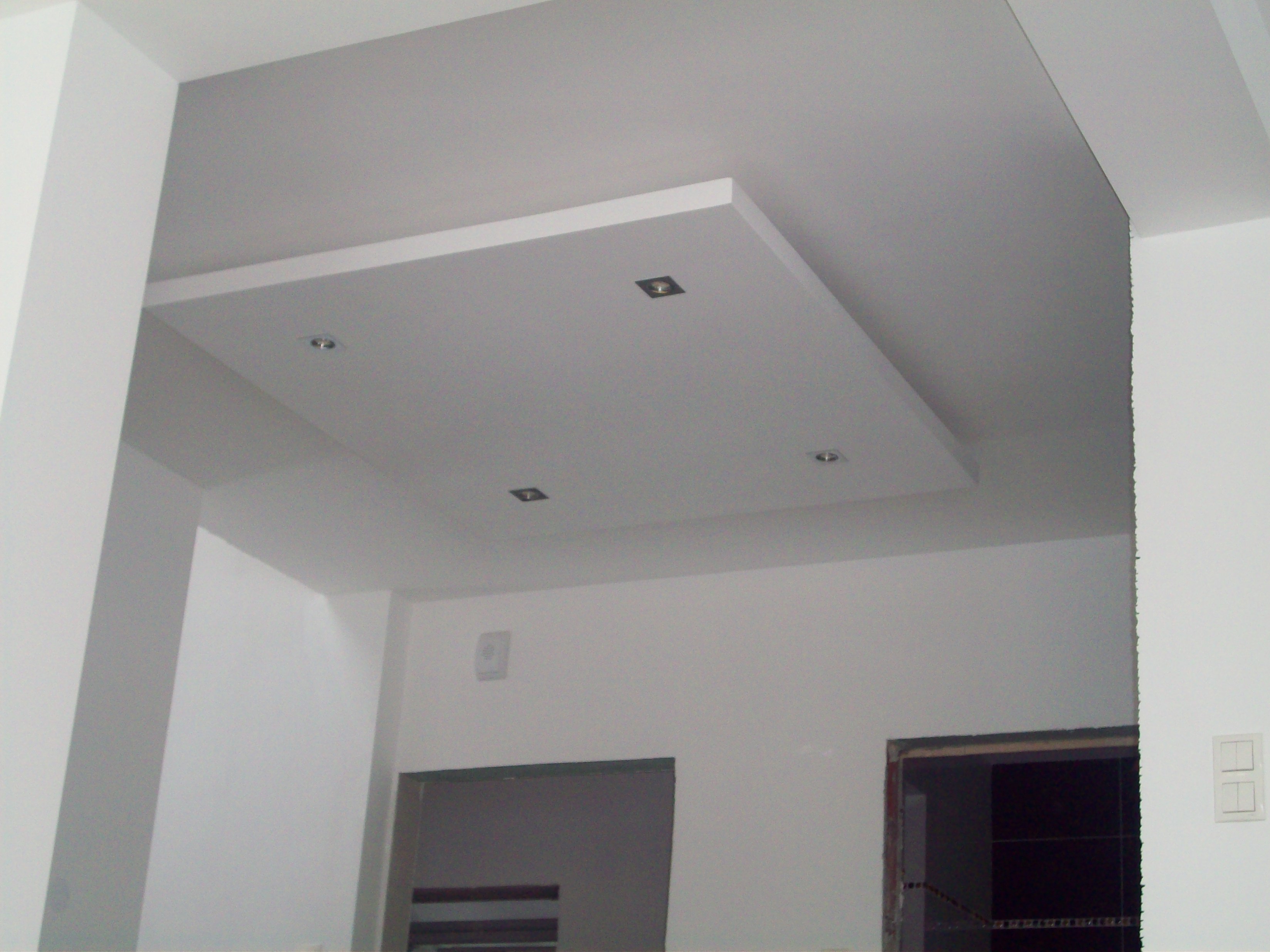 Nowoczesny sufit podwieszany z wbudowanymi punktami świetlnymi, widok z dołu na białe ściany i przygotowane otwory drzwiowe.