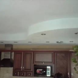 Biały, wielopoziomowy sufit z oświetleniem punktowym w kuchni z zabudową szafek wiszących i okapem.