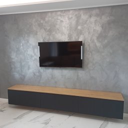 DJW Meble Dariusz Pawlak - Szara szafka RTV z blatem drewnianym pod wiszącym telewizorem na ścianie z efektem betonu. Nowoczesne wnętrze z marmurową podłogą i listwą przypodłogową.