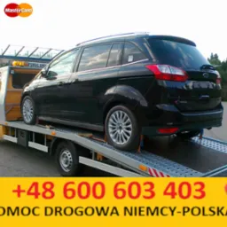 Żółta laweta z czarnym Fordem C-Max na platformie, widoczne logo Visa i Mastercard, numer telefonu i napis 'Pomoc Drogowa Niemcy-Polska' na żółtym tle.