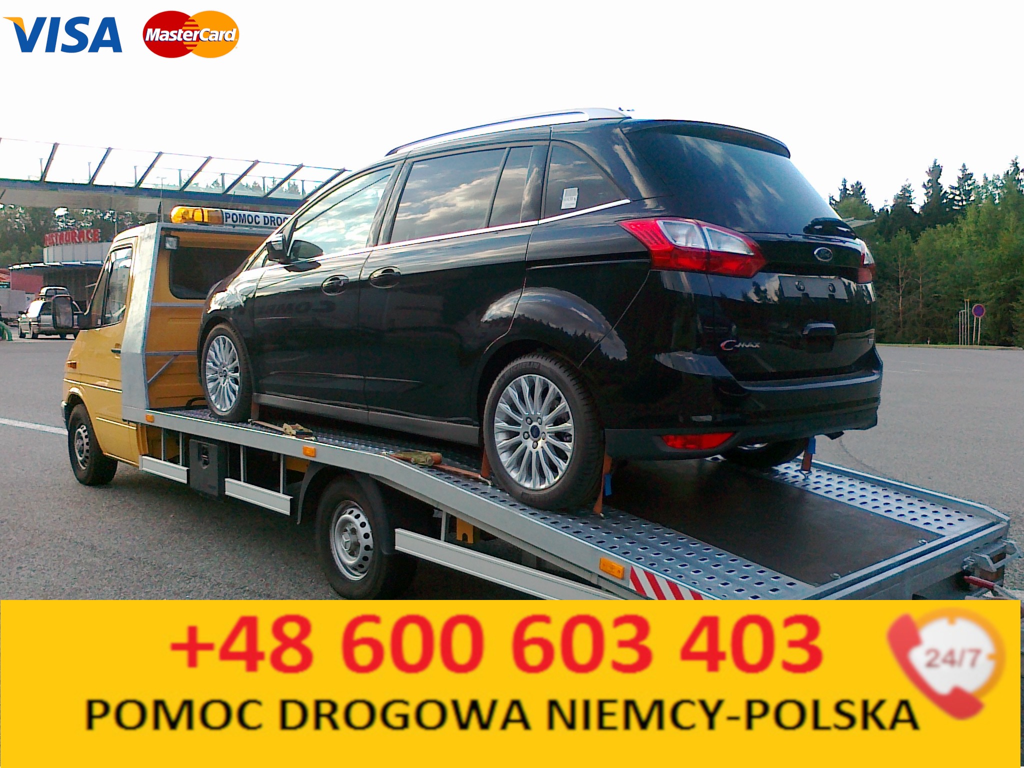 Żółta laweta z czarnym Fordem C-Max na platformie, widoczne logo Visa i Mastercard, numer telefonu i napis 'Pomoc Drogowa Niemcy-Polska' na żółtym tle.