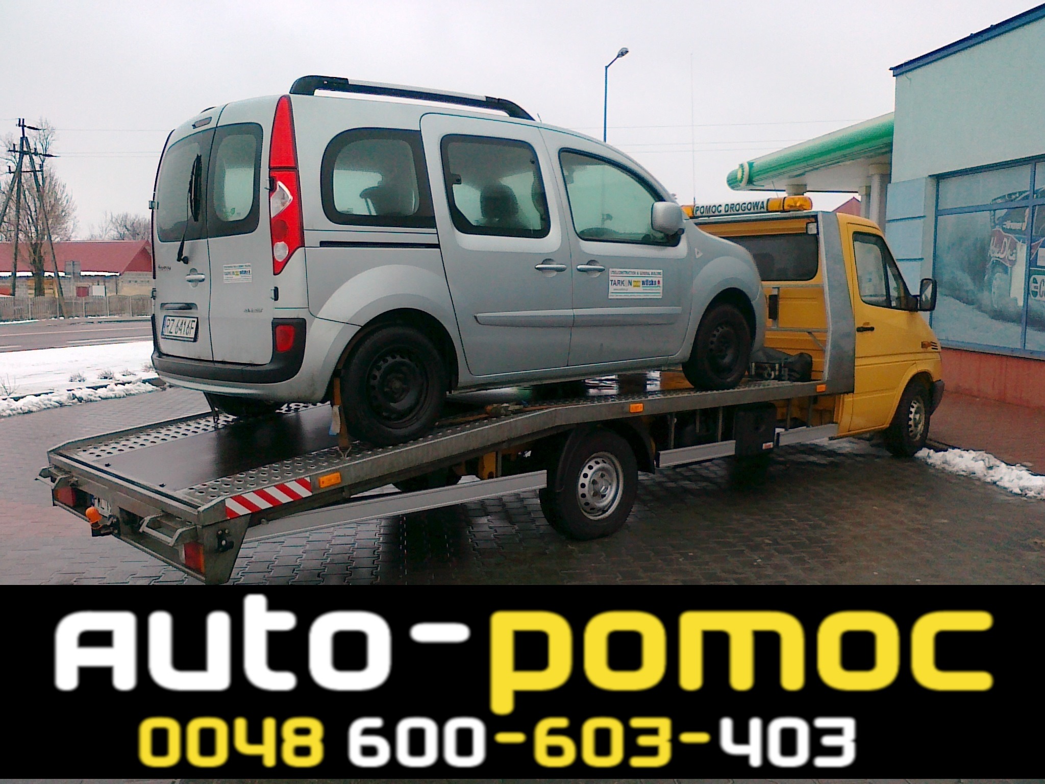 Srebrny samochód dostawczy Renault Kangoo z tablicą rejestracyjną RZ 4416F transportowany na żółtej lawecie pomocy drogowej na tle stacji benzynowej.
