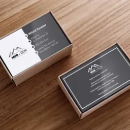 Dwa pudełka wizytówkowe firmy budowlanej Mur-Dom na drewnianym biurku, jedno z danymi kontaktowymi, drugie z zakresem usług: budowa domów, hal, rozbiórki, wykopy, usługi koparką.