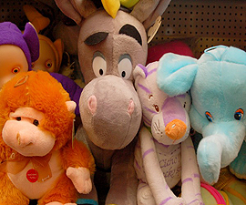 Grupka pluszowych zabawek: szary osiołek z żółtym rogiem, pomarańczowa małpka z czerwoną etykietą, fioletowy tygrysek z niebieskimi uszami i jasnoniebieski słonik, stłoczone razem na półce.