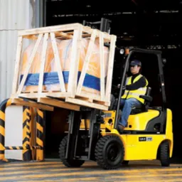 Żółty wózek widłowy Hyundai 18D-7E przewozi paletę z ładunkiem w drewnianej skrzyni, operator w kamizelce odblaskowej