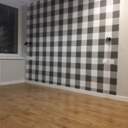 Pokój z drewnianą podłogą i ścianą w szaro-białą kratę, oświetloną przez lampę sufitową i kinkiety