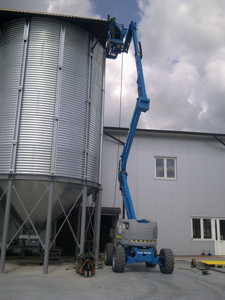 Prace wysokościowe przy silosie zbożowym z użyciem podnośnika koszowego Genie Boom, widoczny pracownik w koszu na wysokości.