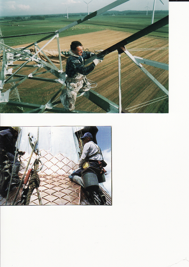Dwóch mężczyzn na wysokościach: jeden maluje konstrukcję stalową wieży w oddali widoczne turbiny wiatrowe, drugi montuje metalową siatkę na ścianie budynku.