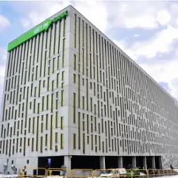 Nowoczesny biurowiec z zielonym logo 'GET IN BANK' na dachu, widziany z dołu pod kątem, z kilkoma samochodami i fragmentem parkingu na pierwszym planie.