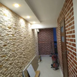 Korytarz po remoncie z dekoracyjną ścianą z kamienia i cegły. Widoczne oświetlenie sufitowe i akcesoria budowlane.