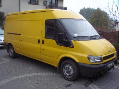 Żółty samochód dostawczy Ford Transit na brukowanym podjeździe, widok z przodu i boku, z widocznym logo Forda na masce.